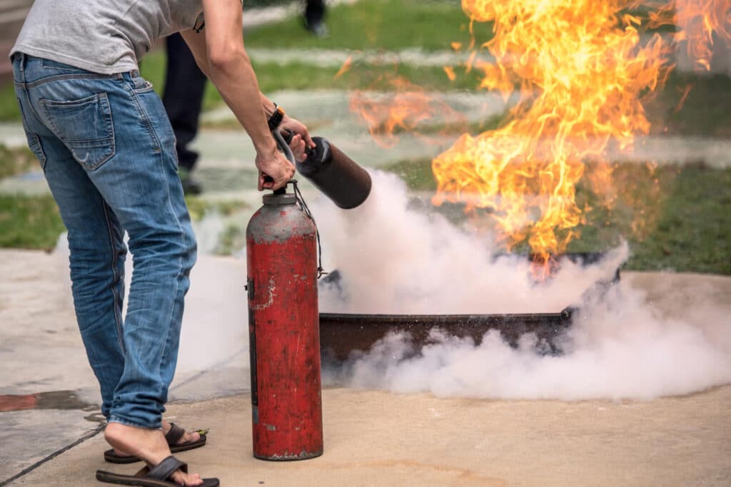 un homme en jeans et tshirt gris qui éteint un incendie avec un extincteur pendant une formation pour devenir équipier de première intervention.