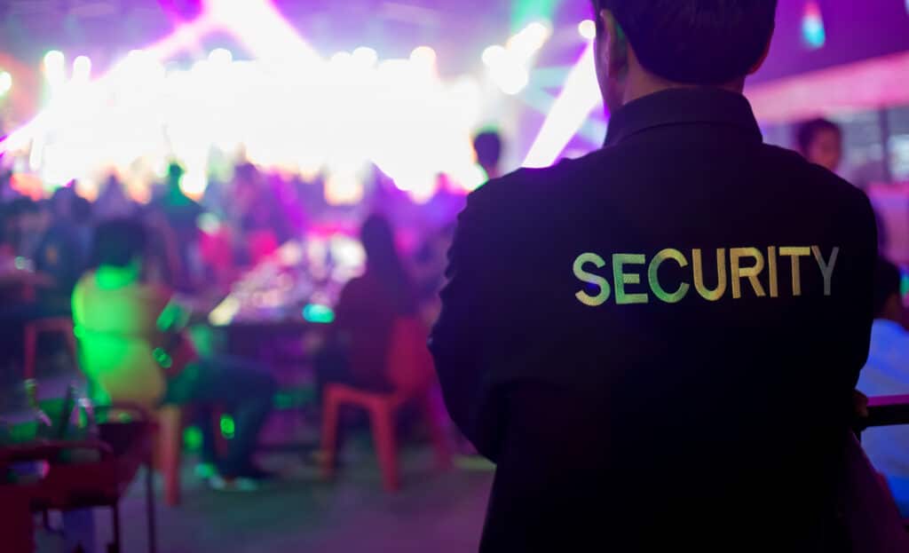 un agent de sécurité boite de nuit avec un blouson security vu de dos qui surveille la foule