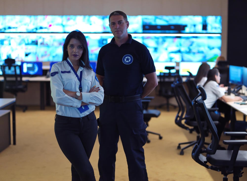 deux manager sécurité debout dans une salle de contrôle, avec des écrans en arrière plan